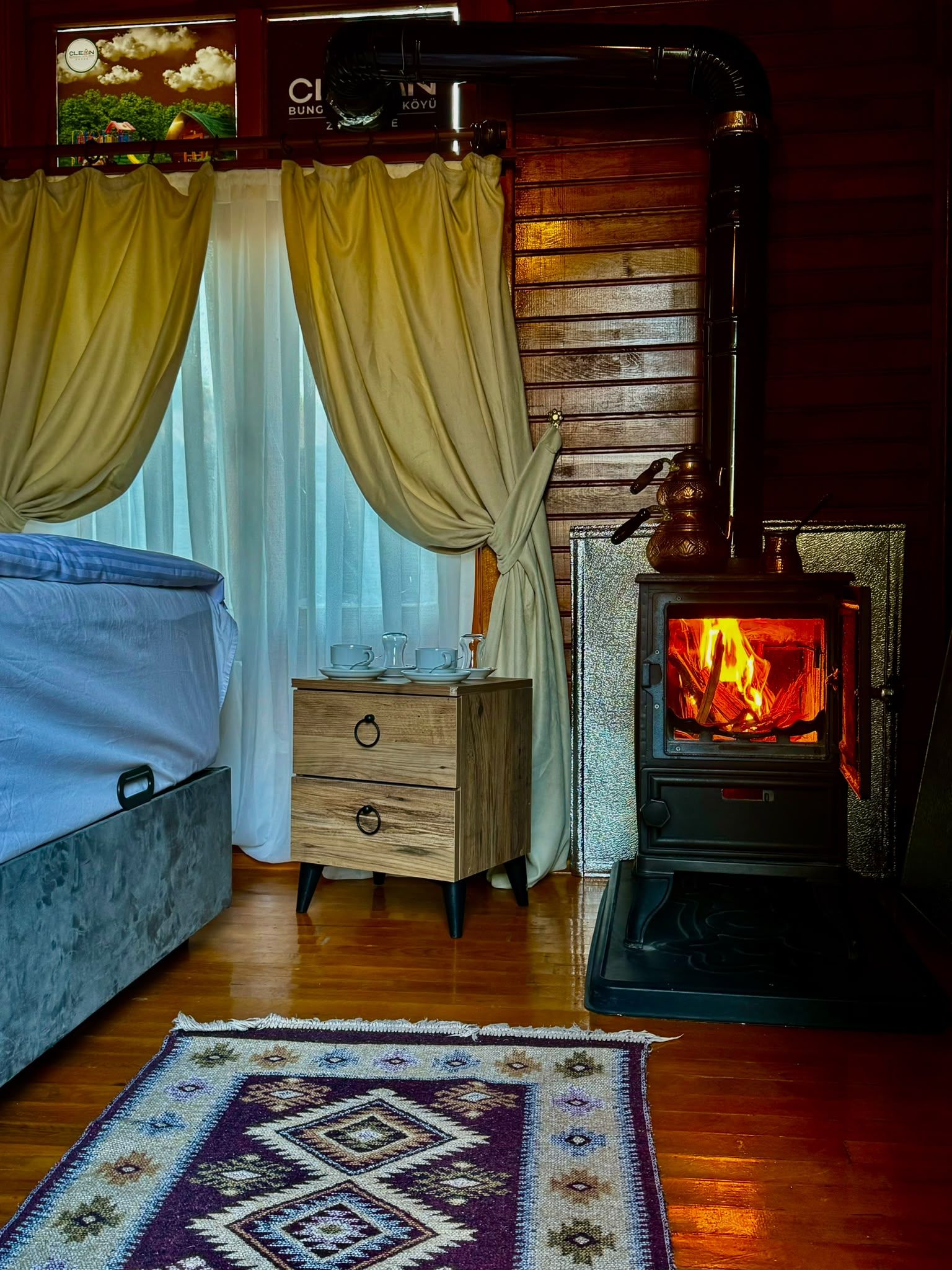 Una habitación acogedora con una cama, un aparador de madera, una alfombra estampada y una estufa de leña.