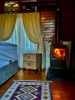 A cozy room with a bed, a wooden dresser, a patterned rug, and a wood-burning stove.