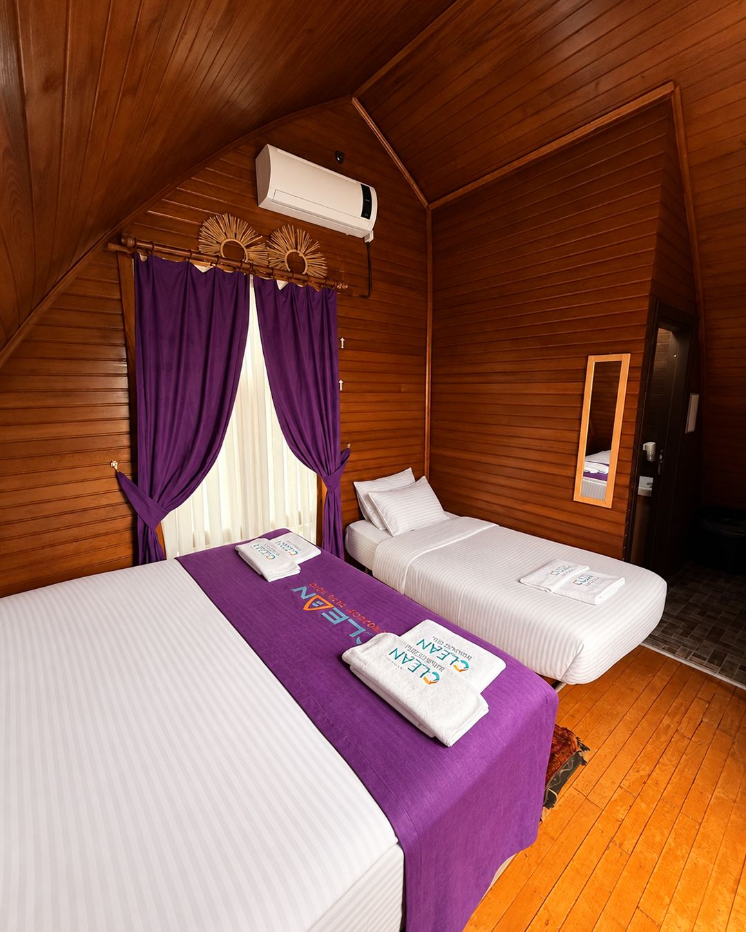 A room with two beds, wooden walls, a ceiling fan, and an air conditioning unit.