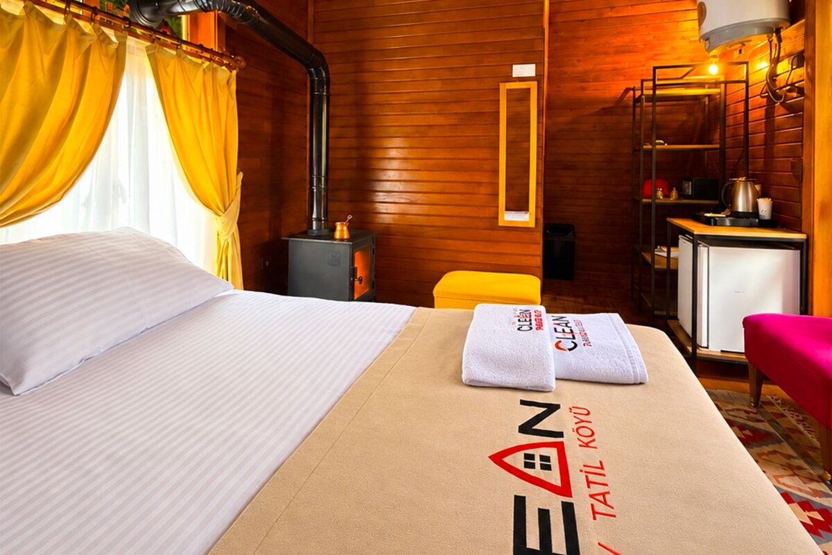 A hotel room with a bed, a heater, a small table, a chair, and a towel with the hotel name.
