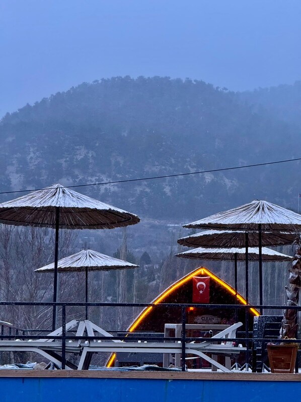 A building with multiple umbrellas, a flag, and a mountainous backdrop.