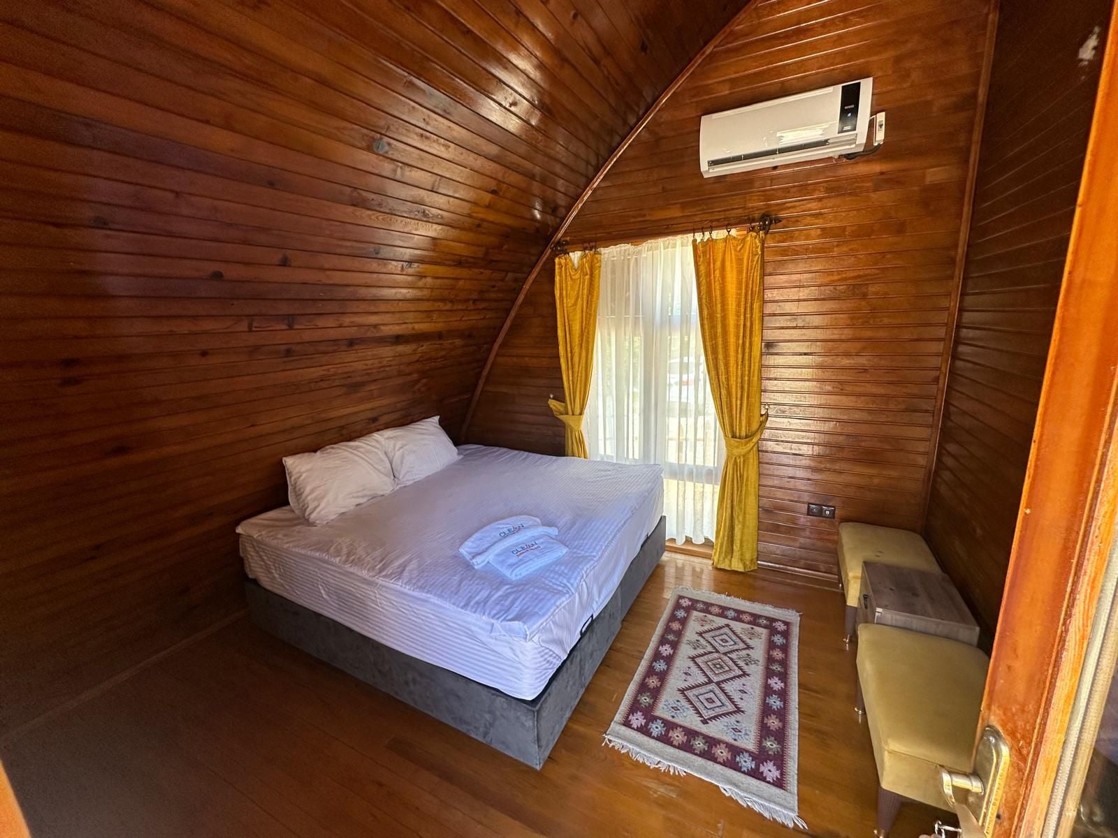 Quarto pequeno com painéis de madeira, uma cama de solteiro, um vaso sanitário e um ar condicionado.