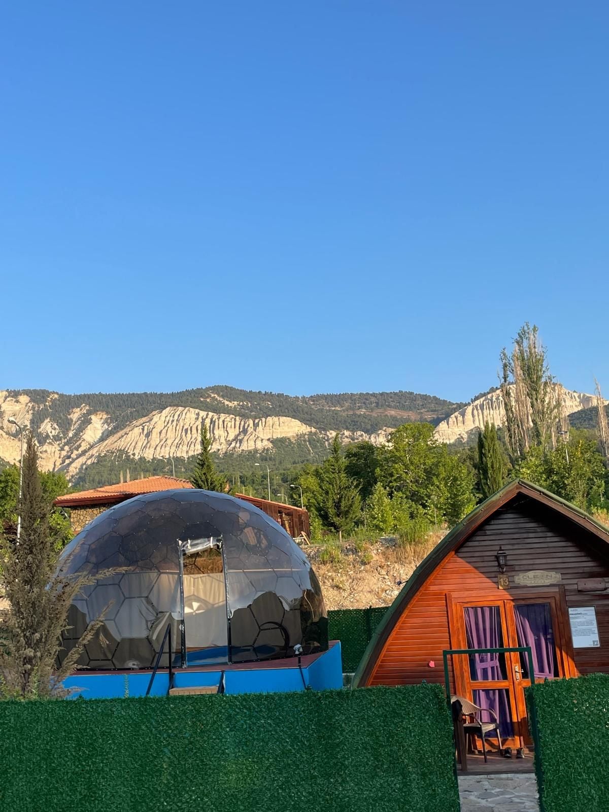 A dome-shaped structure with a wooden cabin adjacent to it, set against a backdrop of mountains and clear sky.