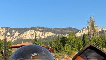 A dome-shaped structure with a wooden cabin adjacent to it, set against a backdrop of mountains and clear sky.