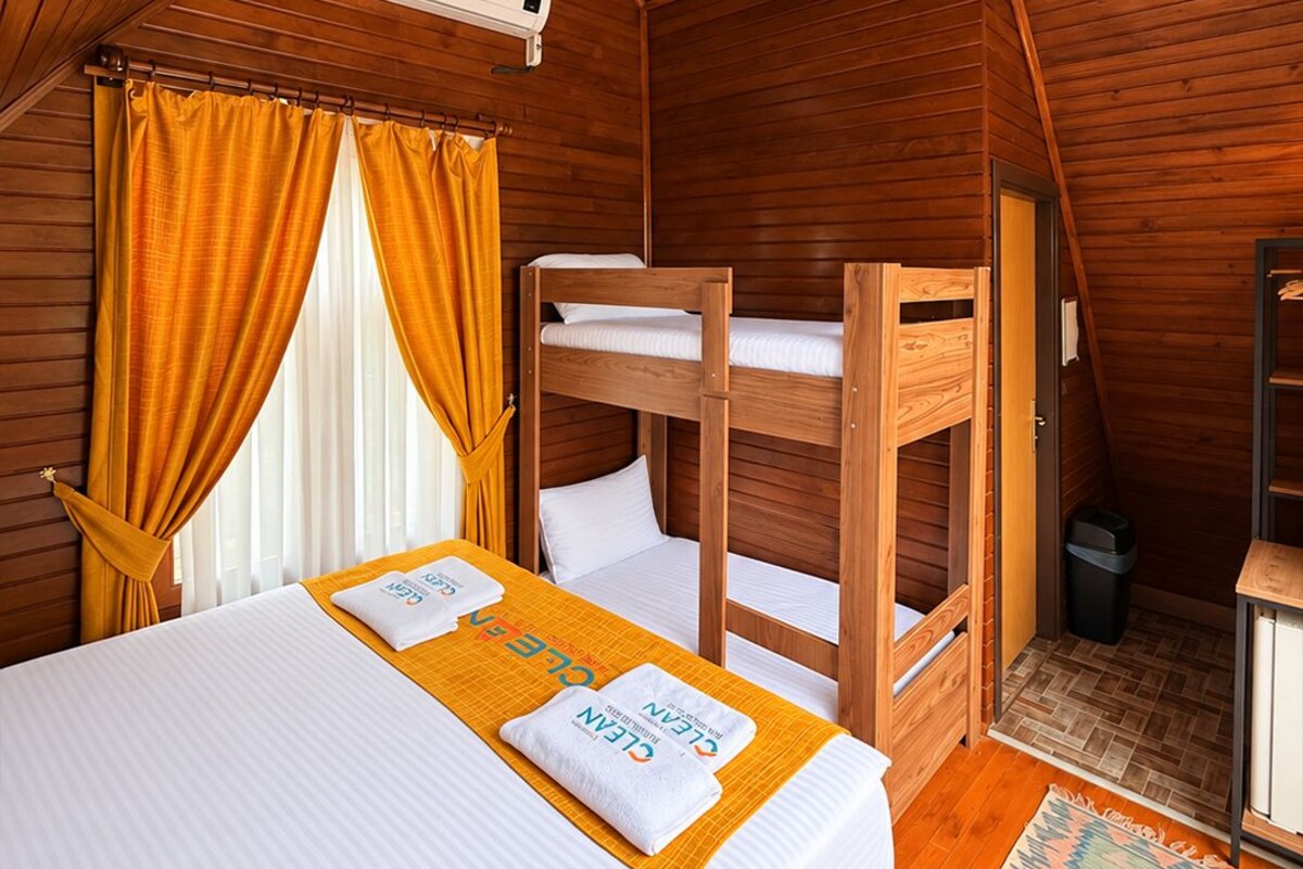 A room with a bunk bed, a single bed, an air conditioning unit, and a small trash bin.