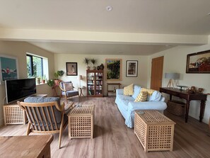 Ein Wohnzimmer mit einer Couch, Sesseln, einem Couchtisch, einem Fernseher und einem Bücherregal.