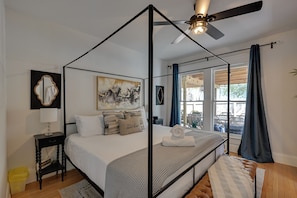 A four-poster bed with a ceiling fan, a bedside table with a lamp, a framed artwork, and a view of the outdoors through a window. - 4BR Tampa Home, Easy Access to Dtwn (Tampa)