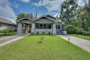 A two-story house with a covered porch, a front yard with grass and a pathway, and a large tree in the background. - 4BR Tampa Home, Easy Access to Dtwn (Tampa)
