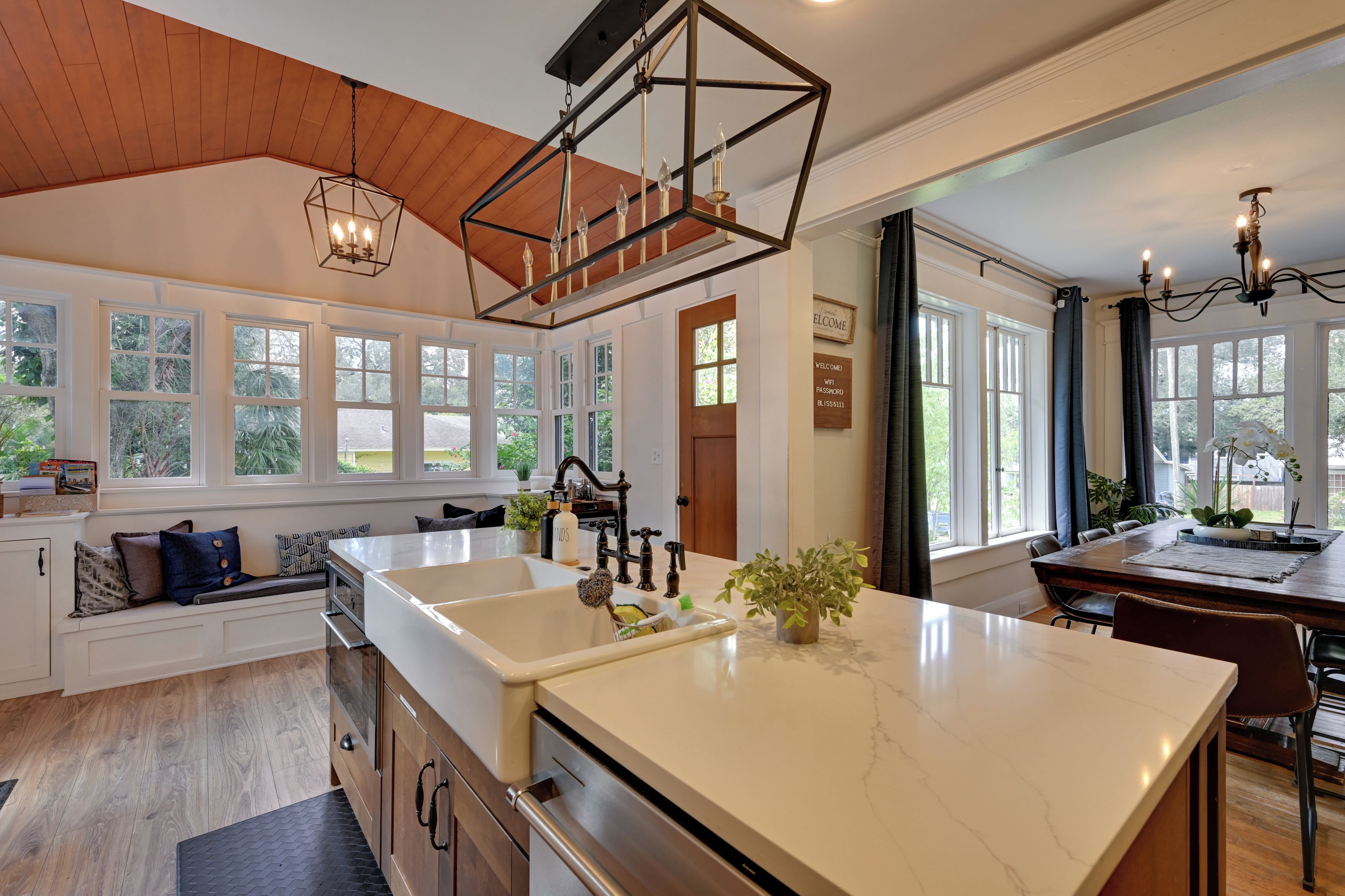 A spacious kitchen with a large island, wooden cabinetry, and a view of the outdoors through large windows.