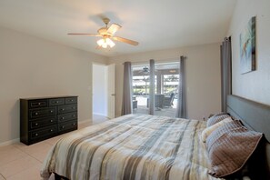 Ein Schlafzimmer mit einem Bett, einem Schminktisch, einem Deckenventilator und Blick durch eine Glastür.