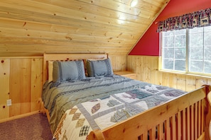 A wooden cabin bedroom with a sloped ceiling, a bed with patterned bedding, and a window with a plaid curtain. - Cabin w/ Jacuzzi 1 Mi From Bear Mountain Ski (Big Bear Lake)