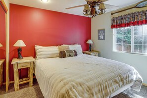 A bedroom with a large bed, two bedside tables, a ceiling fan, a window with plaid curtains, and a wall with a bear-themed sign. - Cabin w/ Jacuzzi 1 Mi From Bear Mountain Ski (Big Bear Lake)