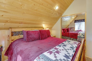 A bedroom with a wooden ceiling, a bed with red bedding, a nightstand, and a mirror reflecting the room. - Cabin w/ Jacuzzi 1 Mi From Bear Mountain Ski (Big Bear Lake)