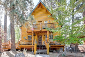 A two-story log cabin with a porch, a flag, and a sign welcoming visitors. - Cabin w/ Jacuzzi 1 Mi From Bear Mountain Ski (Big Bear Lake)