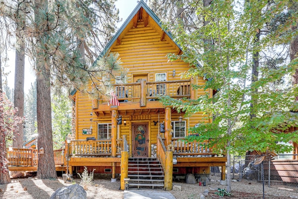 A two-story log cabin with a porch, a flag, and a sign welcoming visitors. - Cabin w/ Jacuzzi 1 Mi From Bear Mountain Ski (Big Bear Lake)