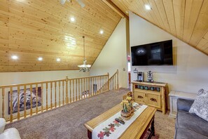A spacious living area with a high ceiling, a wooden staircase, a flat-screen TV mounted on the wall, and a cozy seating area with a sofa and a table. - Cabin w/ Jacuzzi 1 Mi From Bear Mountain Ski (Big Bear Lake)