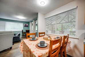Ein Essbereich mit einem Tisch für zwei Personen, Stühlen, einem Fenster mit Jalousien und einer Deckenleuchte.