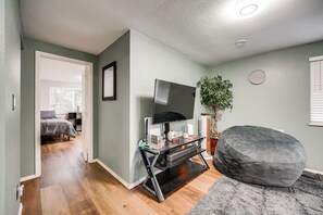 Un salon moderne avec un téléviseur à écran plat, une console de jeux et un fauteuil poire gris.