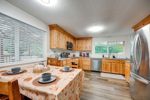 Une cuisine moderne avec des meubles en bois, des appareils en acier inoxydable et un coin repas avec une table dressée pour quatre personnes.