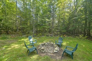 Un espace boisé avec un foyer et trois chaises Adirondack.