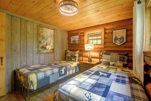 A cabin with two beds, wooden walls, a ceiling fan, and a window. - Maine Log Cabin! Private 2.5-acre Getaway! (Denmark)