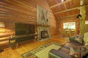 L’intérieur d’une cabane en rondins, avec une télévision, une cheminée, un coin salon et un mur en pierre.