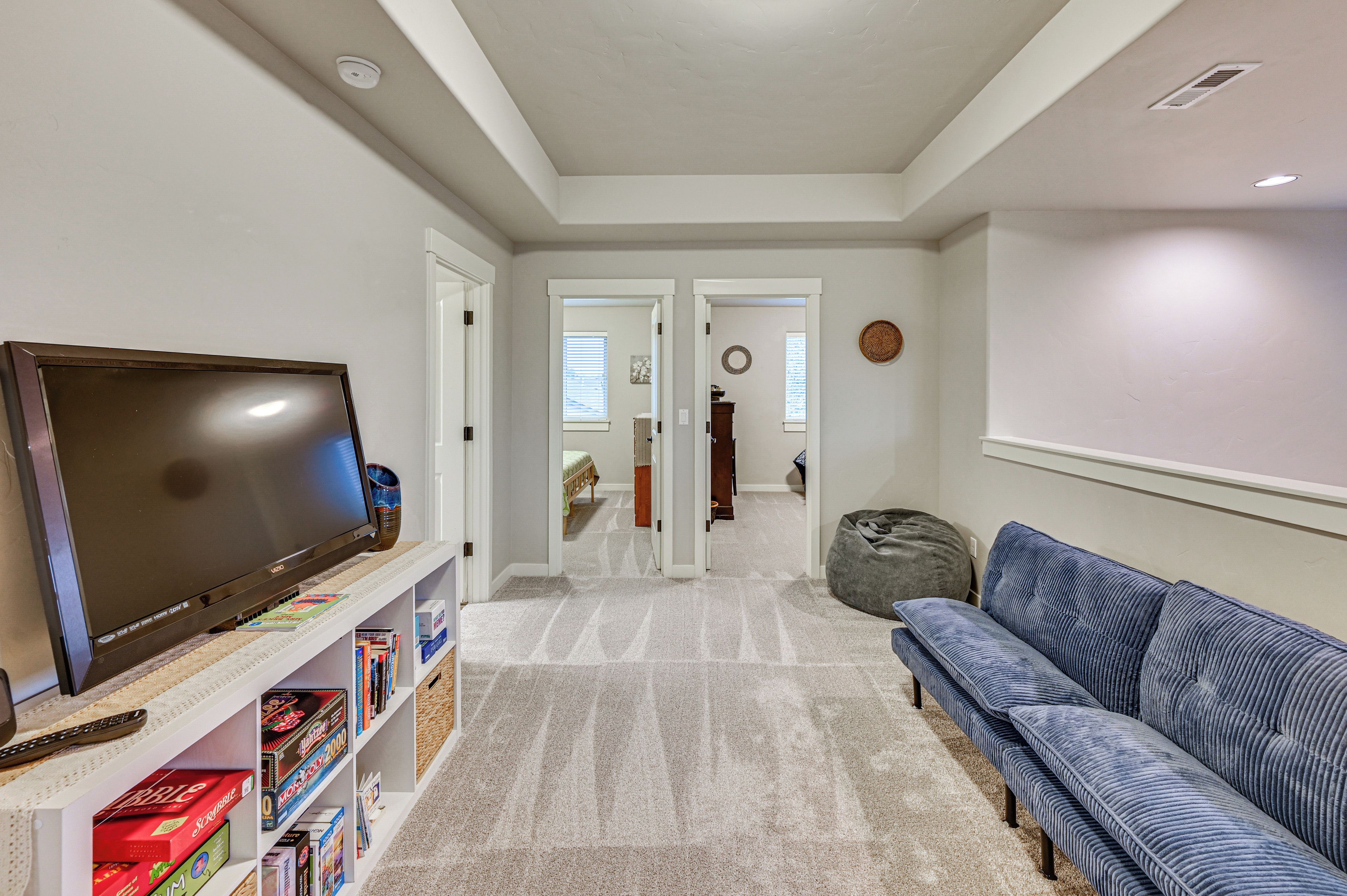 A living room with a flat-screen TV, a bookshelf with board games, a grey bean bag, and a blue sofa.