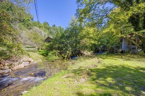 Une maison avec un petit jardin, un ruisseau et un ciel dégagé.