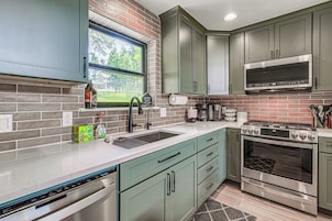 A kitchen with a dishwasher, stove, microwave, and a window with a view of greenery.