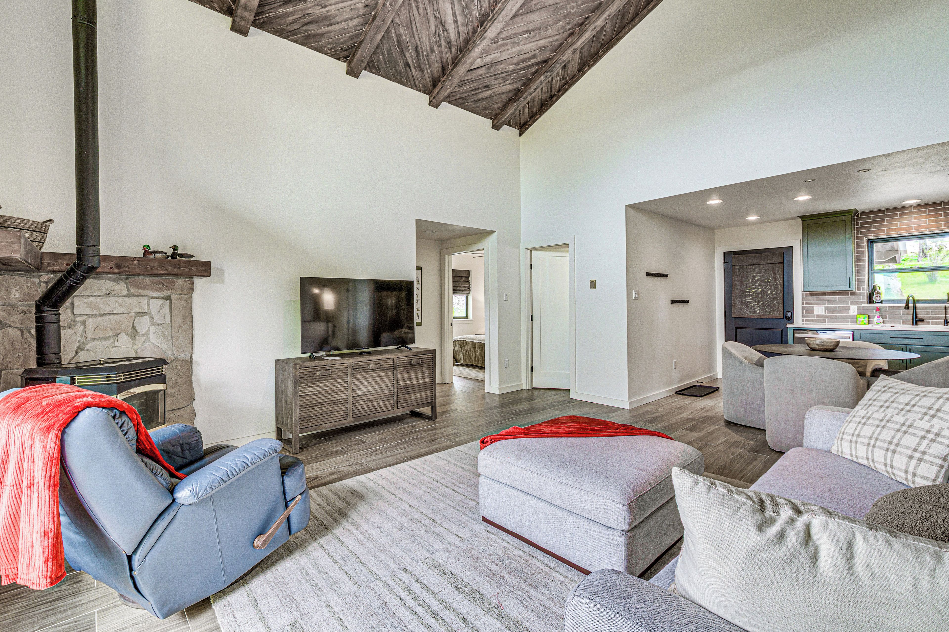 A spacious living area with a stone fireplace, a comfortable seating area with a sofa and ottoman, and a kitchen with a window view.