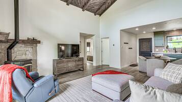 A spacious living area with a stone fireplace, a comfortable seating area with a sofa and ottoman, and a kitchen with a window view.