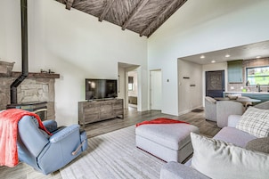 A spacious living area with a stone fireplace, a comfortable seating area with a sofa and ottoman, and a kitchen with a window view.