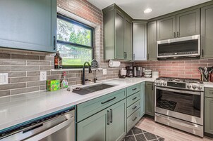 A kitchen with a dishwasher, stove, microwave, and a window with a view of greenery.