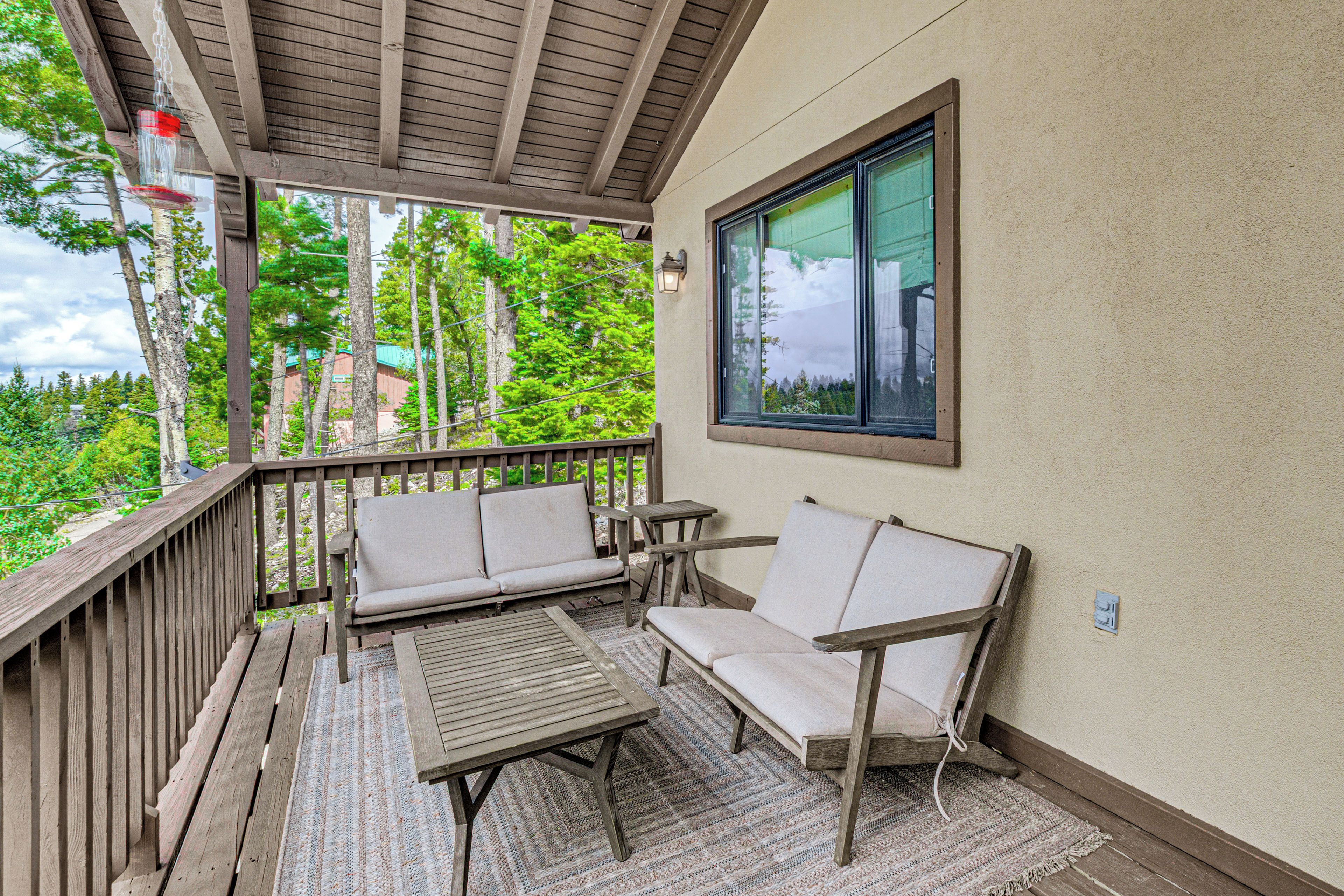 A covered outdoor seating area with a wooden deck, two cushioned chairs, and a small table.