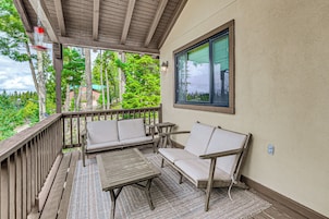 A covered outdoor seating area with a wooden deck, two cushioned chairs, and a small table.
