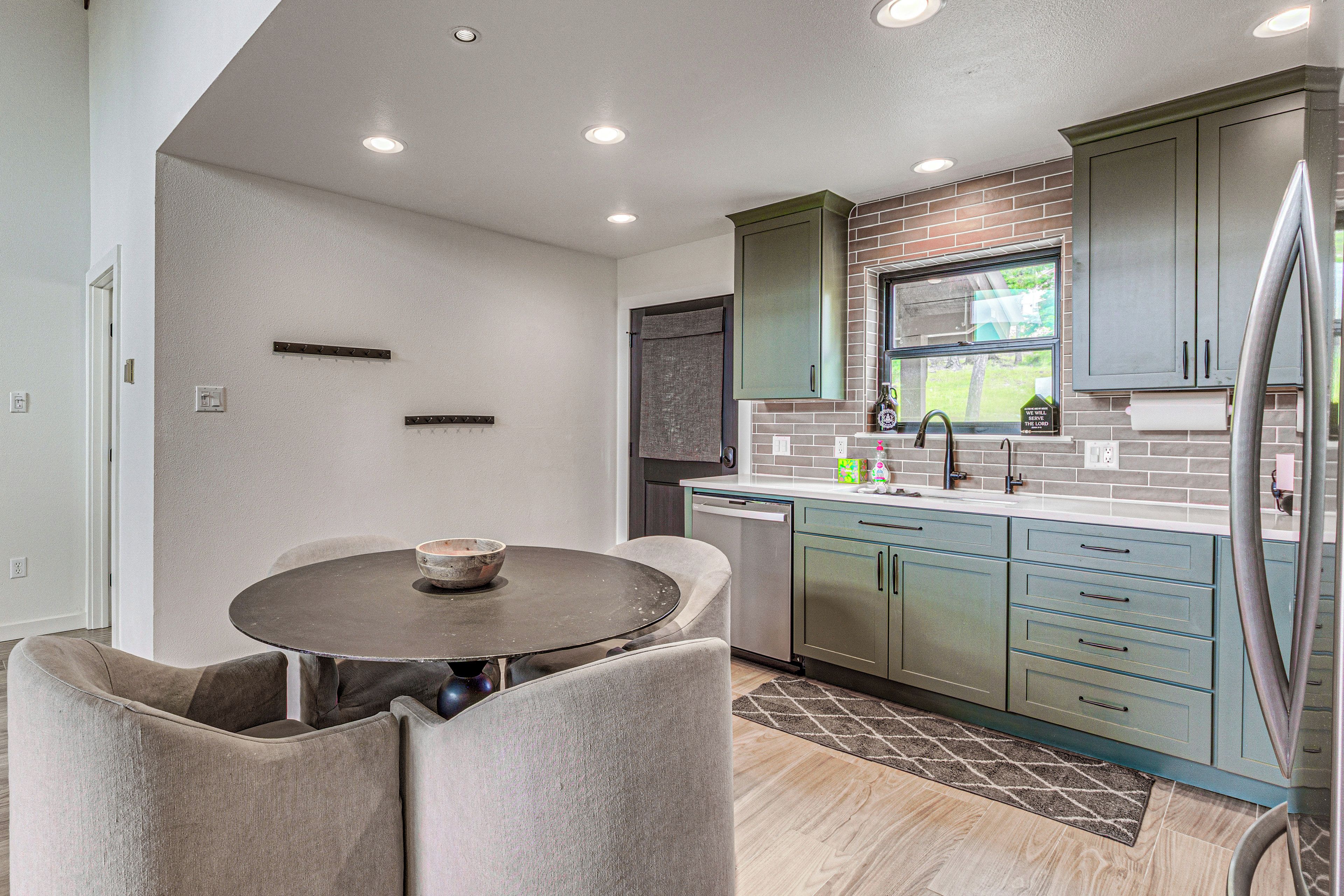 A modern kitchen with a dining area, featuring a round table, grey upholstered chairs, and a built-in dishwasher.