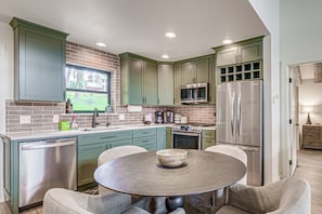 A kitchen with green cabinets, stainless steel appliances, a round table, and a window overlooking a brick wall. - Home Near Ski Cloudcroft & Lincoln Natl Forest! (Cloudcroft)