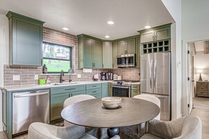 A kitchen with green cabinets, stainless steel appliances, a round table, and a window overlooking a brick wall.