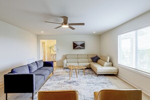 Ein Wohnzimmer mit Deckenventilator, einer Couch, einem Couchtisch und einem Fenster mit Jalousien.