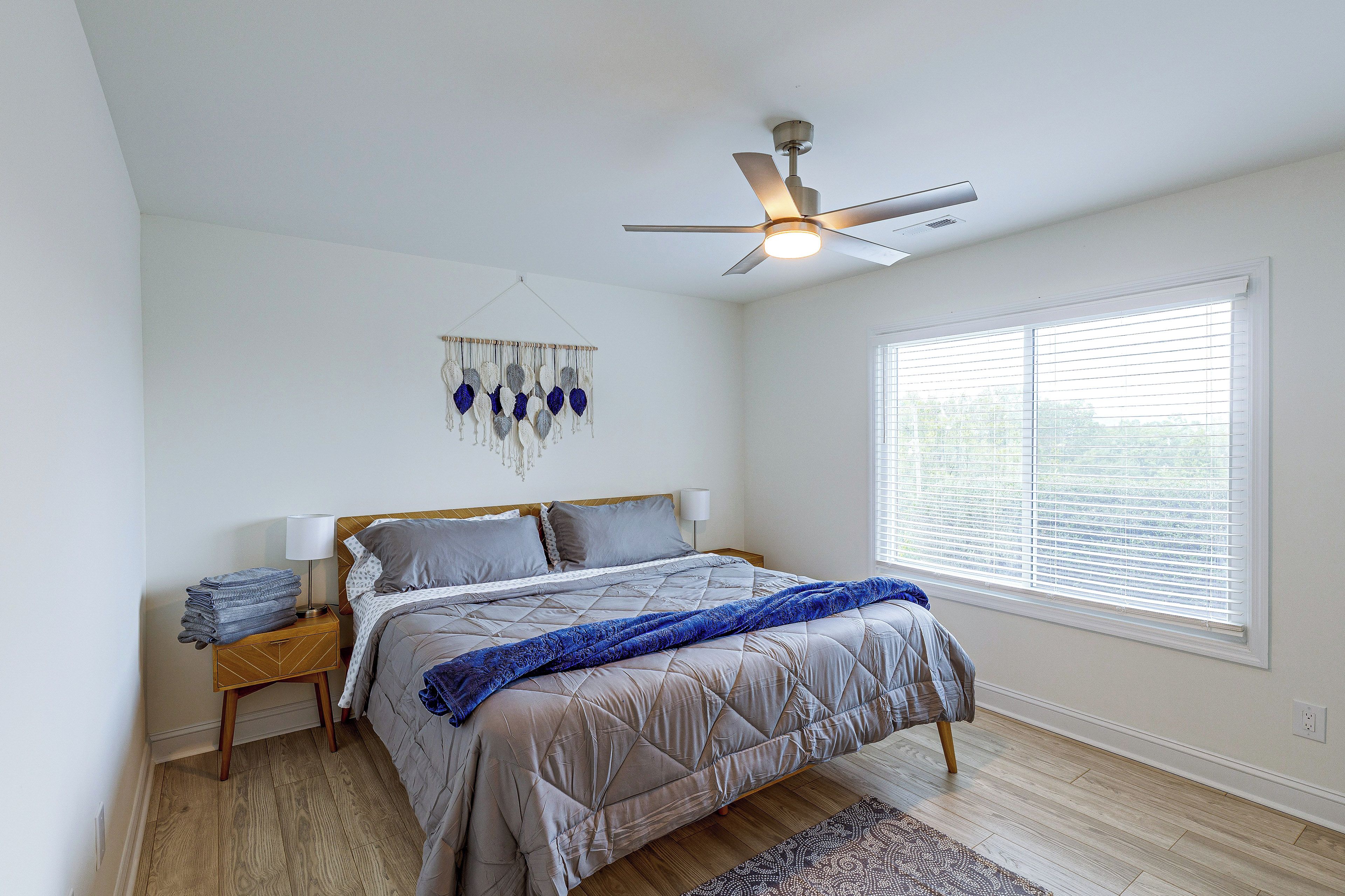 A bedroom with a bed, a ceiling fan, a wall hanging, and a window with blinds.