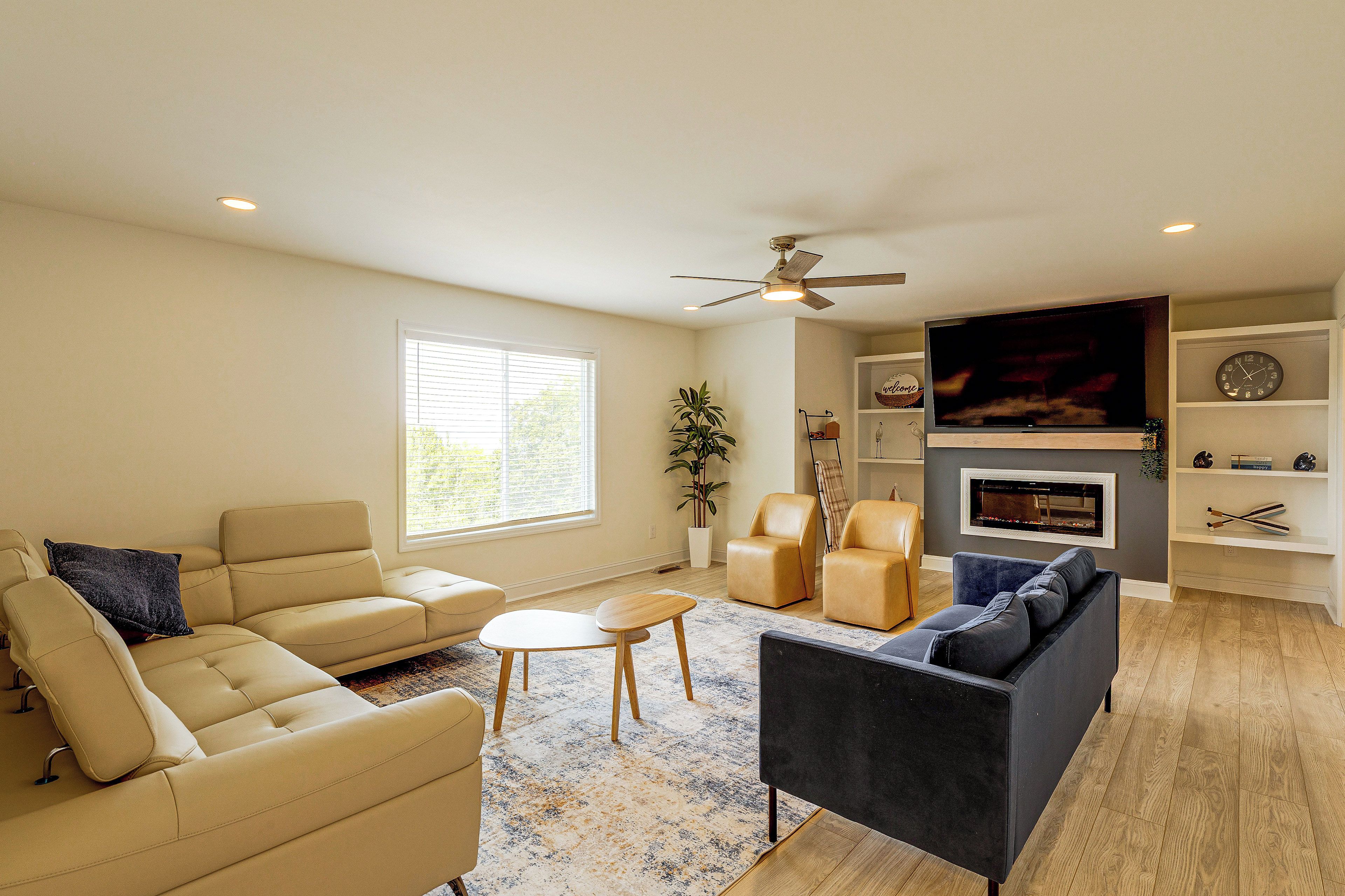 A living room with a sofa, chairs, a television, a fireplace, and a ceiling fan.