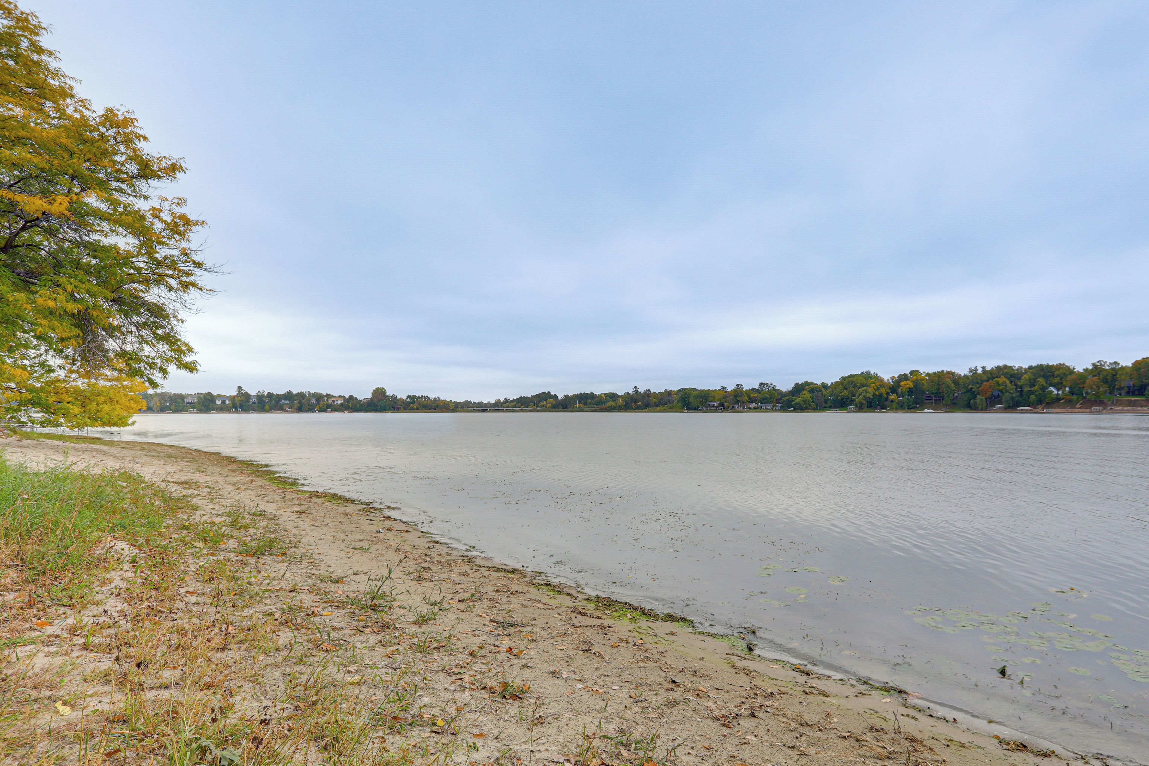 A riverbank with a sandy shore, trees with autumn foliage, and a calm water body.