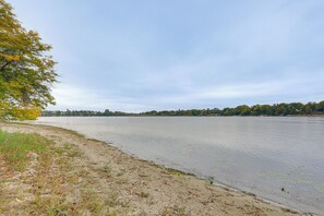 A riverbank with a sandy shore, trees with autumn foliage, and a calm water body. - New! Private Lakefront Retreat on Lindstrom Lake (Lindstrom)