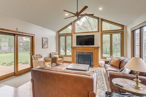 A spacious living room with a fireplace, large windows, and a ceiling fan. - New! Private Lakefront Retreat on Lindstrom Lake (Lindstrom)
