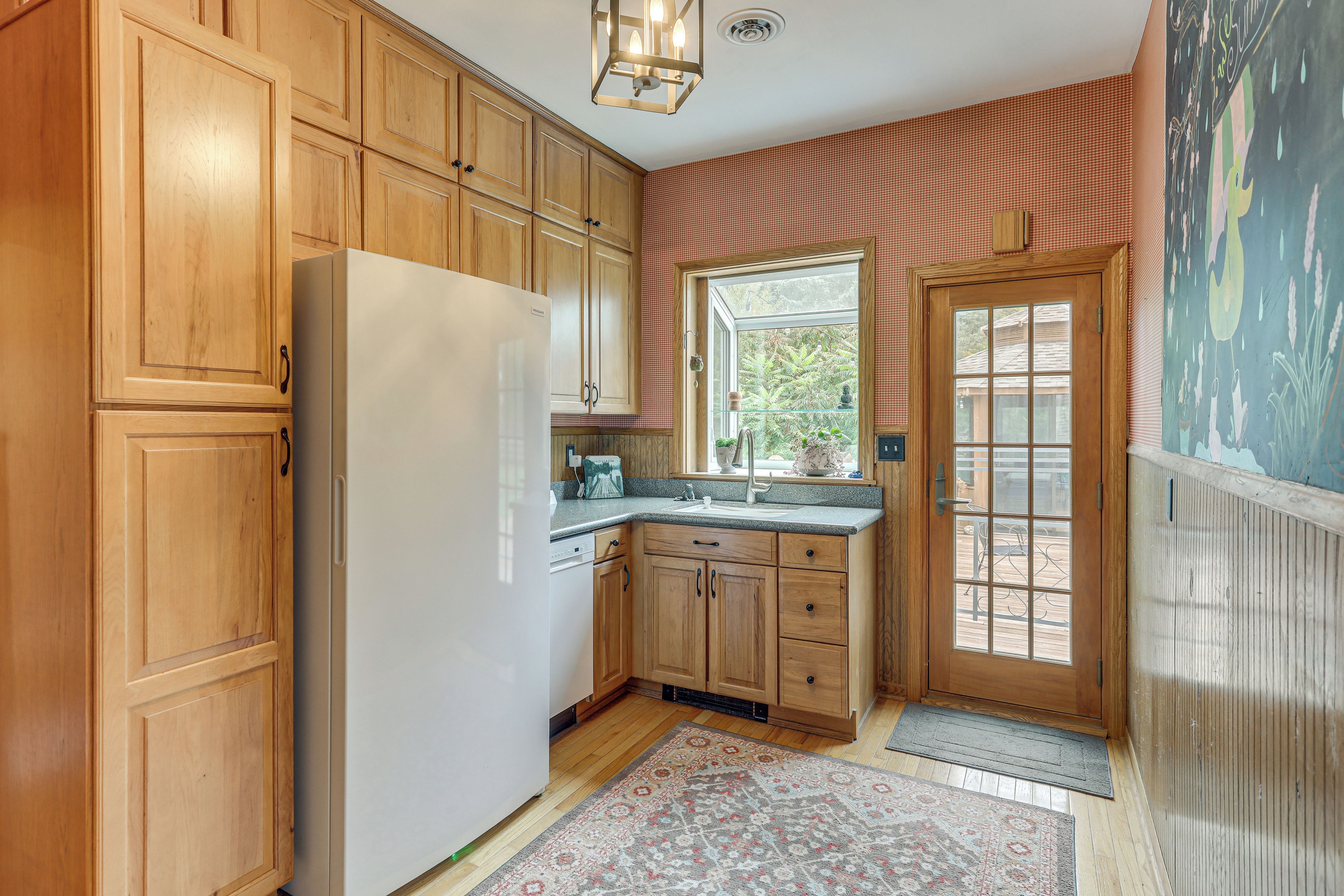 A kitchen with wooden cabinets, a white refrigerator, a window, and a door with a view of the outdoors.