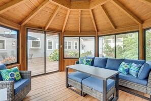 A covered patio area with a wooden ceiling, a table, two wicker sofas with cushions, and large windows offering a view of the backyard. - New! Private Lakefront Retreat on Lindstrom Lake (Lindstrom)
