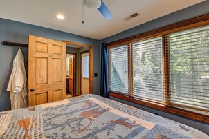 A bedroom with a large window, a wooden door, and a quilt on the bed.