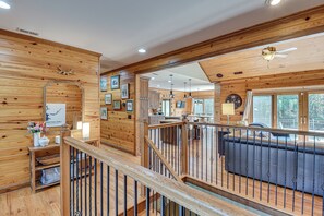 Un interior de madera con una escalera, una sala de estar con sofá y una cocina visible a través de un umbral abierto.