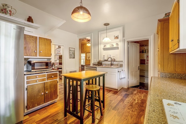 A kitchen with wooden cabinets, a microwave, a wooden table with stools, and a hanging light fixture.