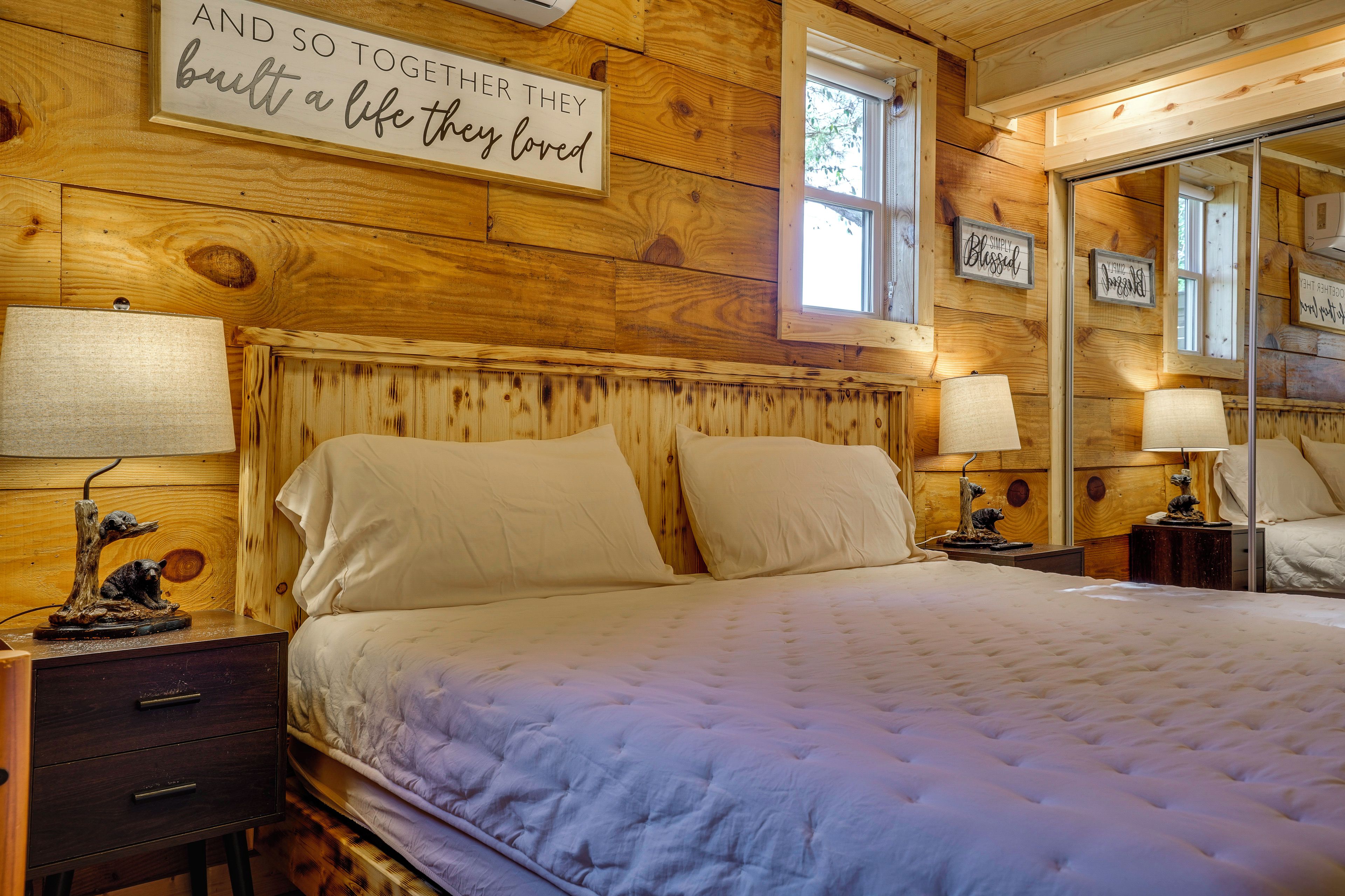 A wooden room with a bed, two bedside tables, a mirror, and wall decorations.